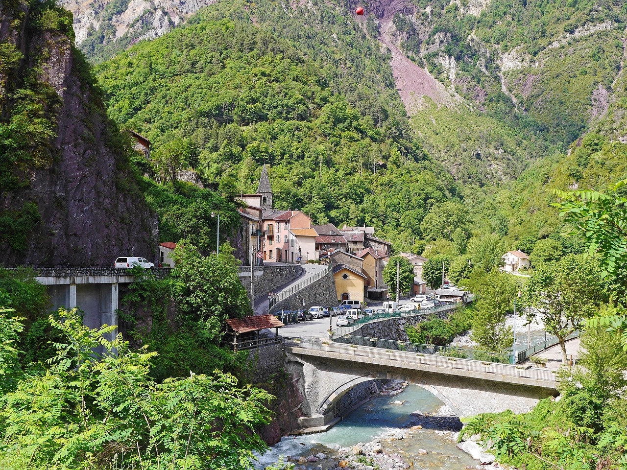 Panorama di un borgo alpino nella Valle Camonica, circondato da montagne e vegetazione estiva.